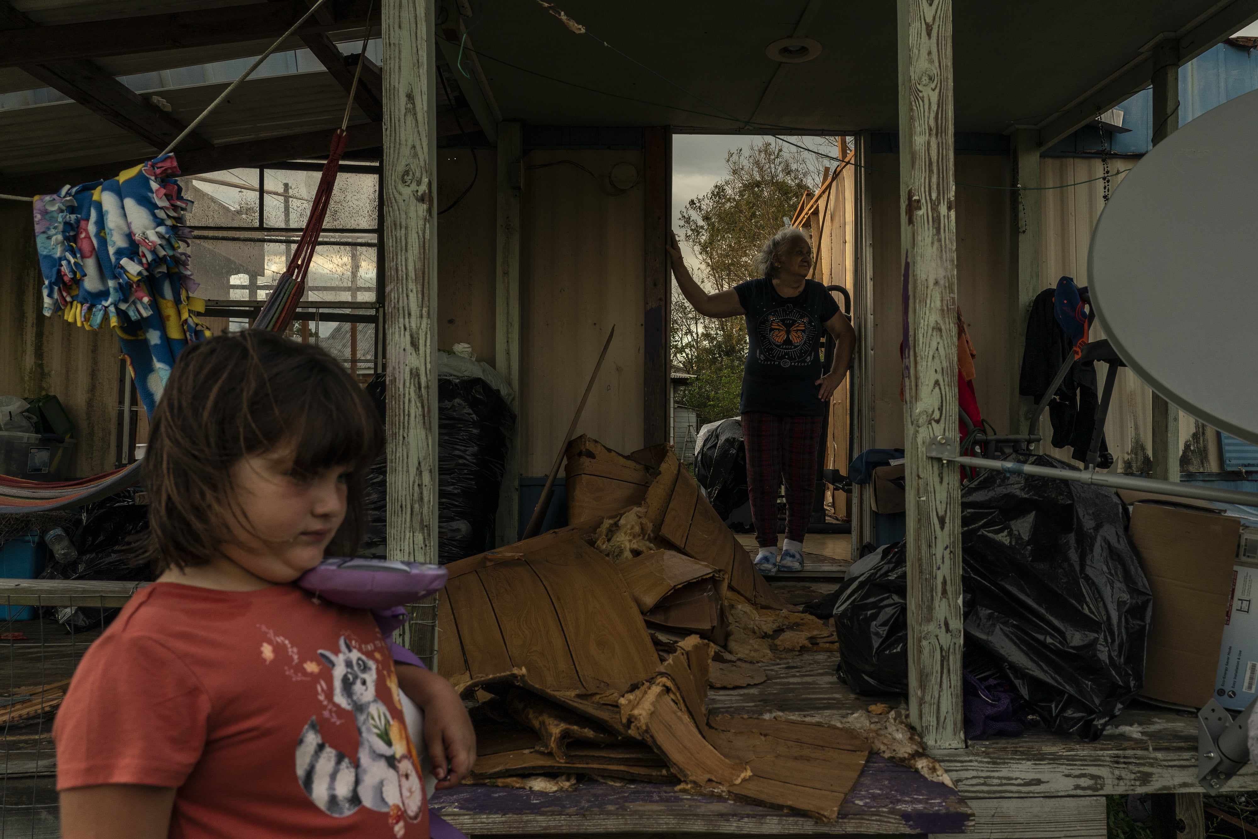 A child stands on the sidelines as her family surveys the damage to their home.